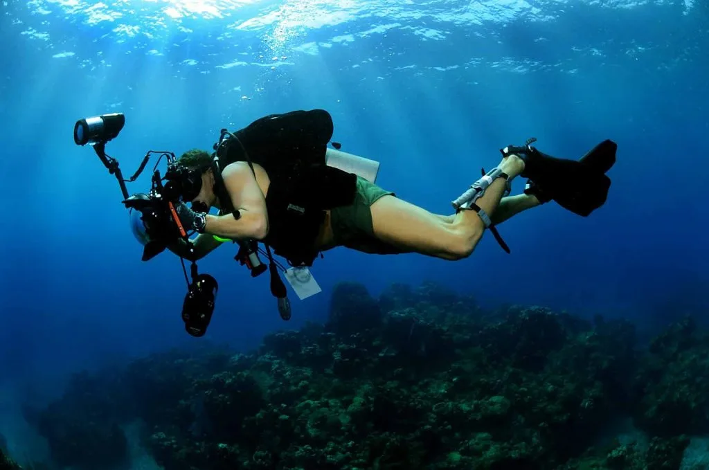 Smiling diver swimming toward the camera with her dive group behind on an Open Water dive