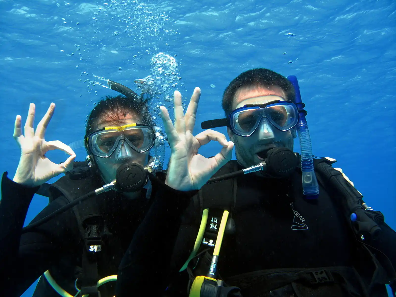 Smiling diver swimming toward the camera with her dive group behind on an Open Water dive