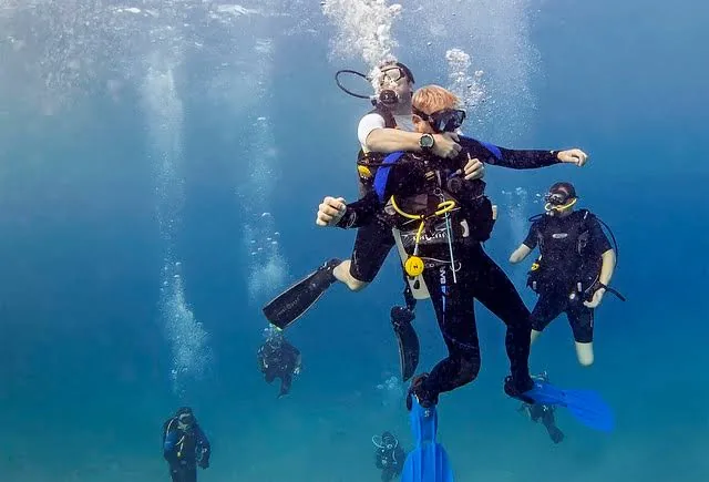 Smiling diver swimming toward the camera with her dive group behind on an Open Water dive